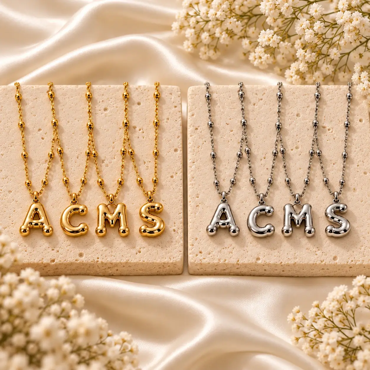 Colliers initiales Bubble A, C, M et S en doré et argenté, présentation premium sur fond crème